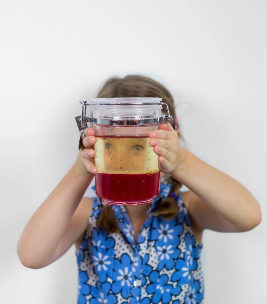 girl looking through a jar of water and oil demonstrating immiscibility.