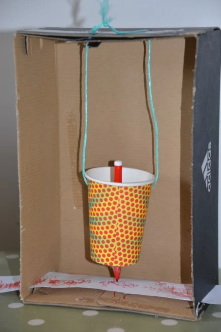 Homemade seismometer using a cardboard box, cup, pencil, string and paper.