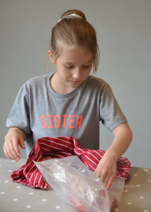 child rolling a bag of ice and salt around another smaller bag filled with smoothie to make a frozen drink.